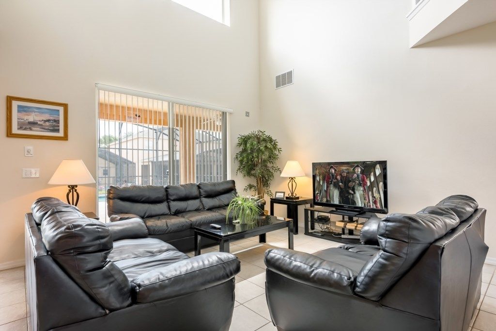 A modern living room with a black leather sofa, a coffee table, a TV, and a large window with blinds.