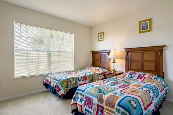 A bedroom with two beds, a nightstand, a lamp, and a window with blinds.