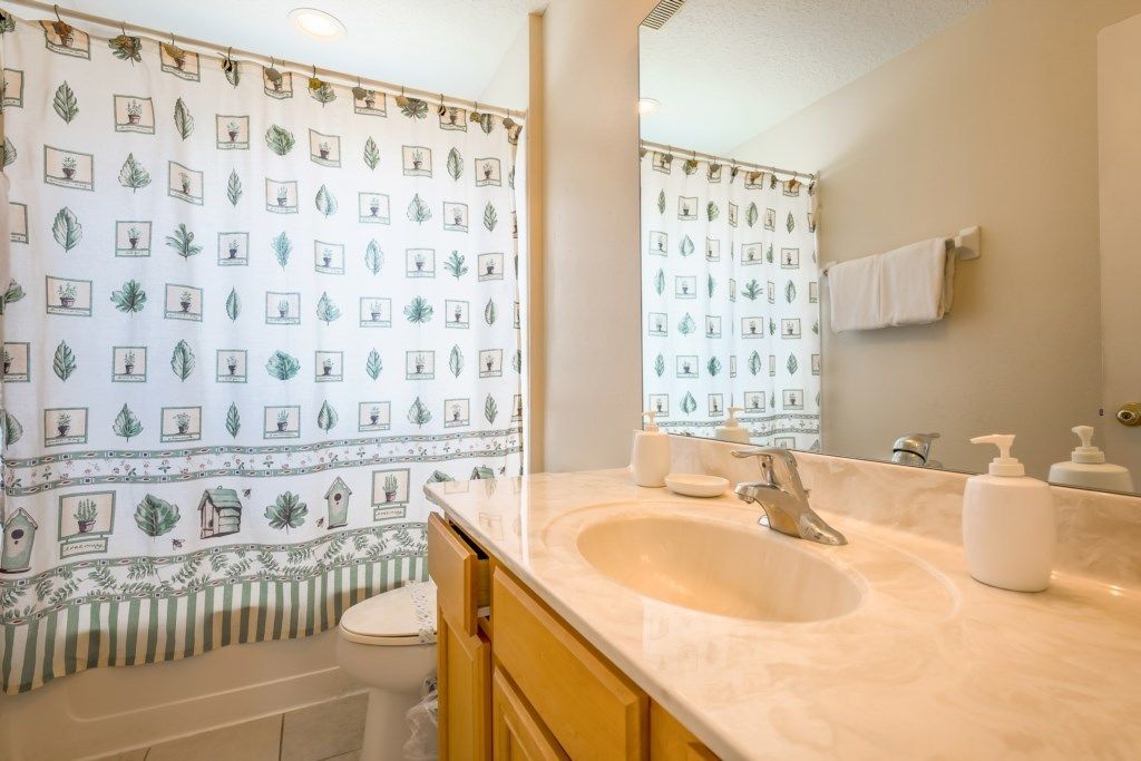 A bathroom with a white sink, a mirror, a toilet, and a shower curtain with a plant pattern.