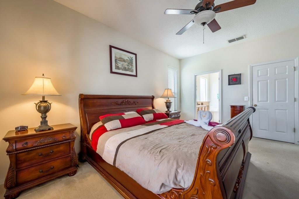 A bedroom with a wooden bed, two bedside tables with lamps, a ceiling fan, and a door.