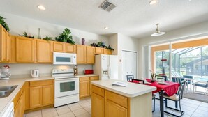 A modern kitchen with wooden cabinets, a central island, and a dining area with a red tablecloth. - 7BR Pool Home Emerald Island by SHV-2793 (Kissimmee)