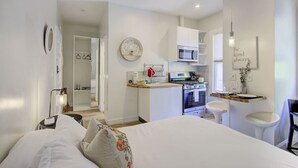 Un dormitorio moderno y luminoso con una cama grande, un pequeño kitchenette y un baño visible a través de una puerta abierta.