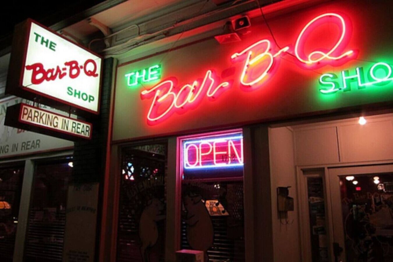 A storefront with neon signs for "The Bar-B-Q Shop" and "The Bar-B-Q S.H.O." and a sign indicating "PARKING IN REAR".