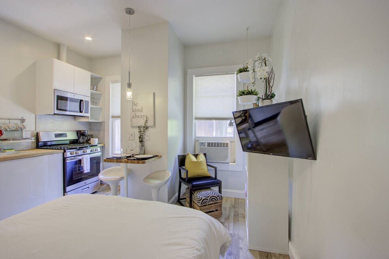 Une chambre compacte comprenant un lit, une petite kitchenette, un coin repas et un téléviseur fixé au mur.