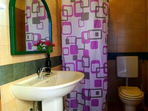 Een badkamer met een witte wastafel, een toilet en een douchegordijn met een geometrisch patroon.