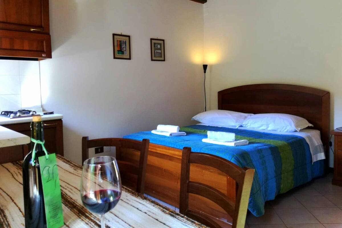 Ein Hotelzimmer mit einem Bett, einem Holz-Kopfteil, einem Nachttisch, einem Tisch mit einer Weinflasche und einem Glas sowie einer Lampe.