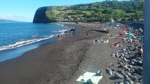 A beach with dark sand, people sunbathing, and a large cliff in the background. - Azores Beach Home for adults/children, 3 bed.2 bath, First Fl., 3534/AL (Horta, Azores)