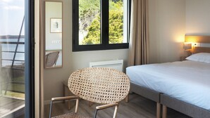 A hotel room with a bed, a rocking chair, a window with a view of trees, a ceiling light, and a wall-mounted air conditioner.