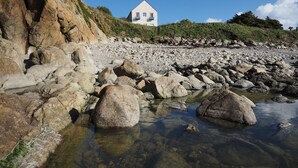 A coastal landscape with a white house on a cliff, rocky shoreline, and clear water.