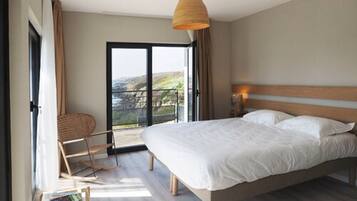 Une chambre avec un grand lit, une chaise, une petite table et une vue sur l’extérieur grâce à une porte coulissante.