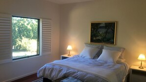 Ein Schlafzimmer mit großem Fenster, einem Bild an der Wand und zwei Nachttischlampen.