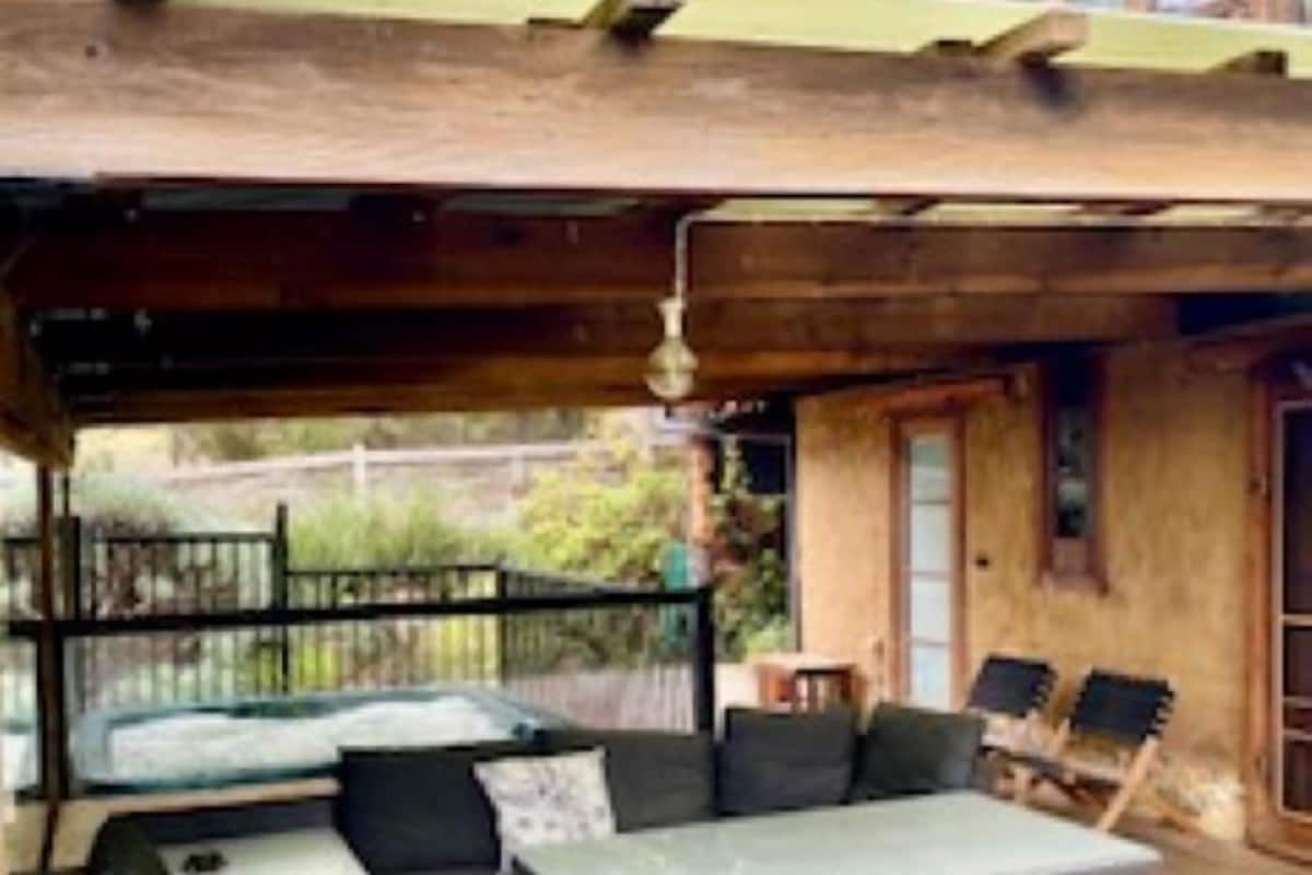 An outdoor seating area with a wooden deck, a covered section, and a view of the surrounding greenery.