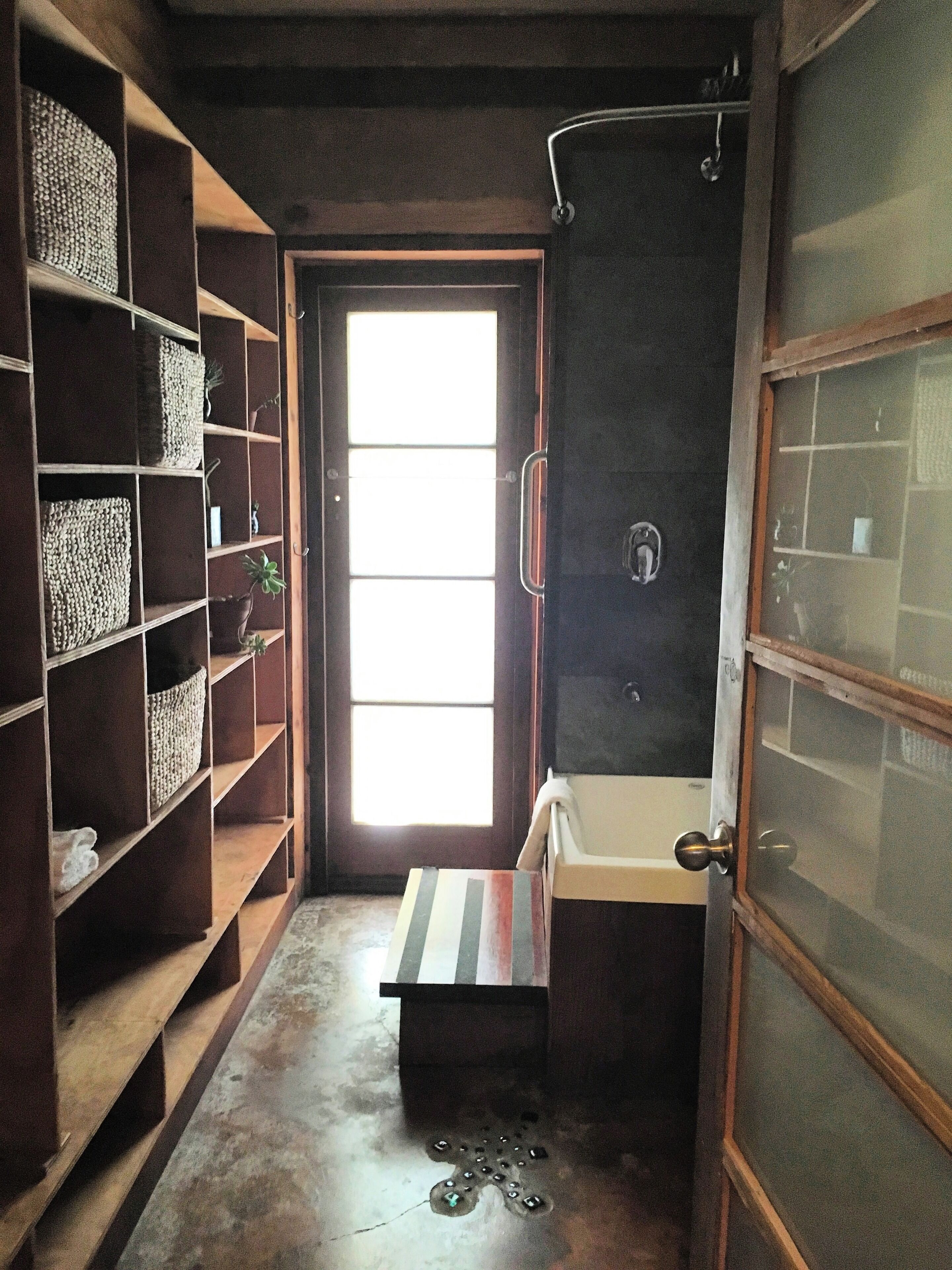 Un baño estrecho con ducha, lavamanos y repisas con cestas.