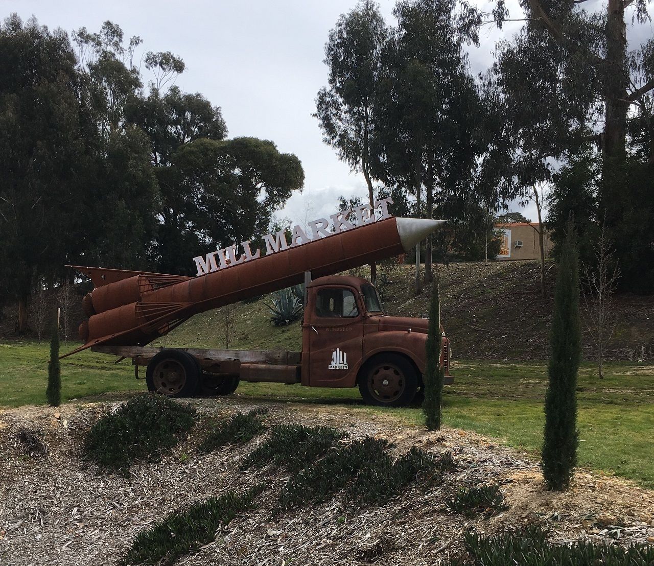 Un camion d'epoca con un grande serbatoio cilindrico su un rimorchio, parcheggiato in zona erbosa con alberi e un edificio sullo sfondo.