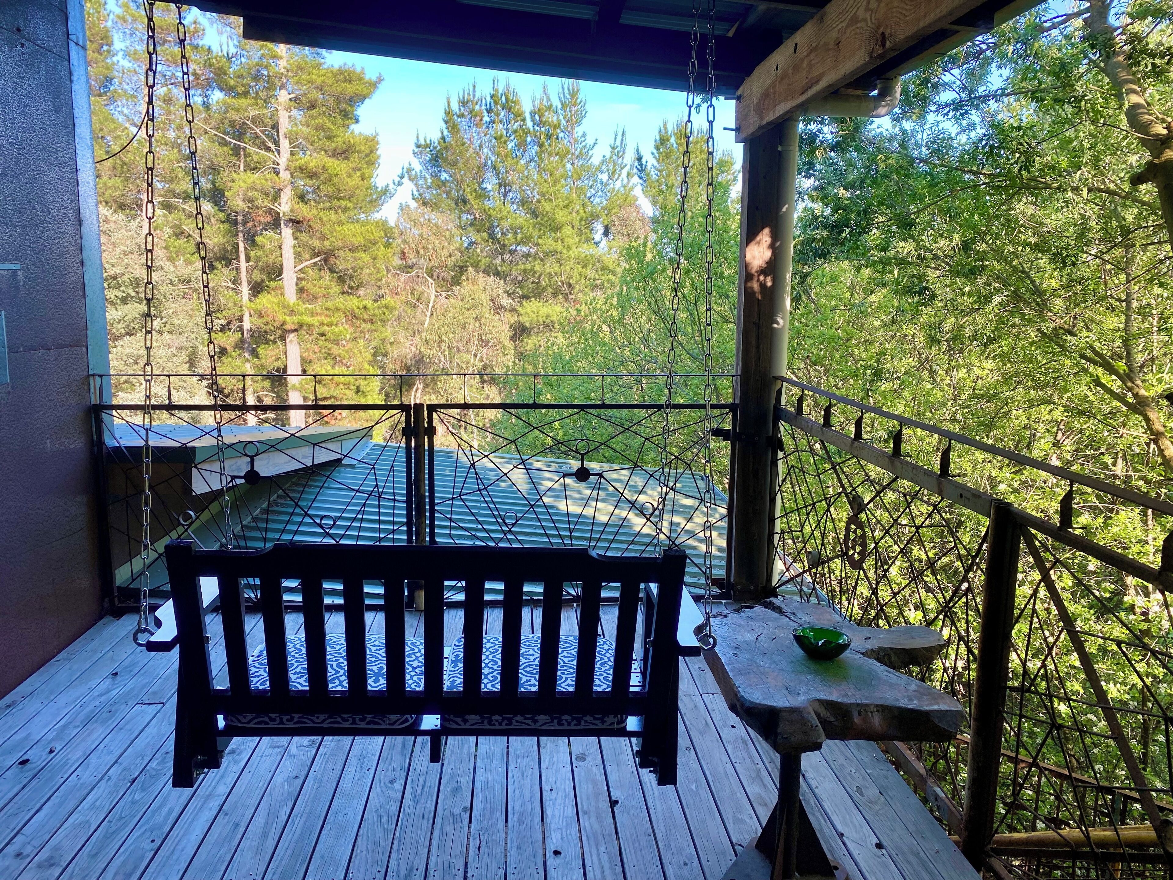 Terraza de madera con un banco y una mesa, con vistas a un área boscosa.