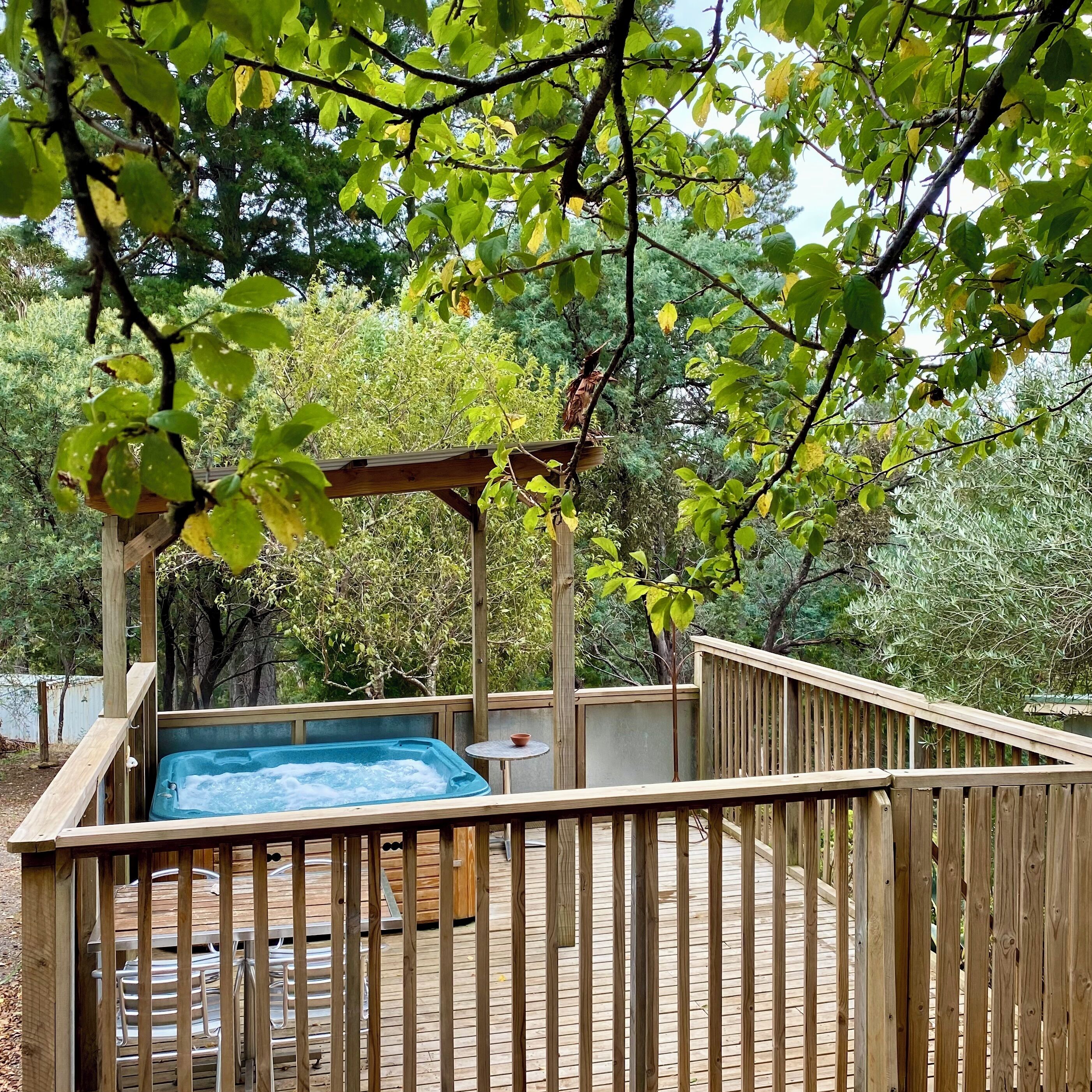 A wooden deck with a hot tub, surrounded by a wooden fence and trees.