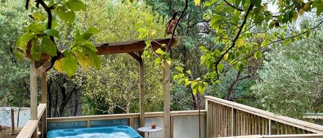 A wooden deck with a hot tub, surrounded by a wooden fence and trees.