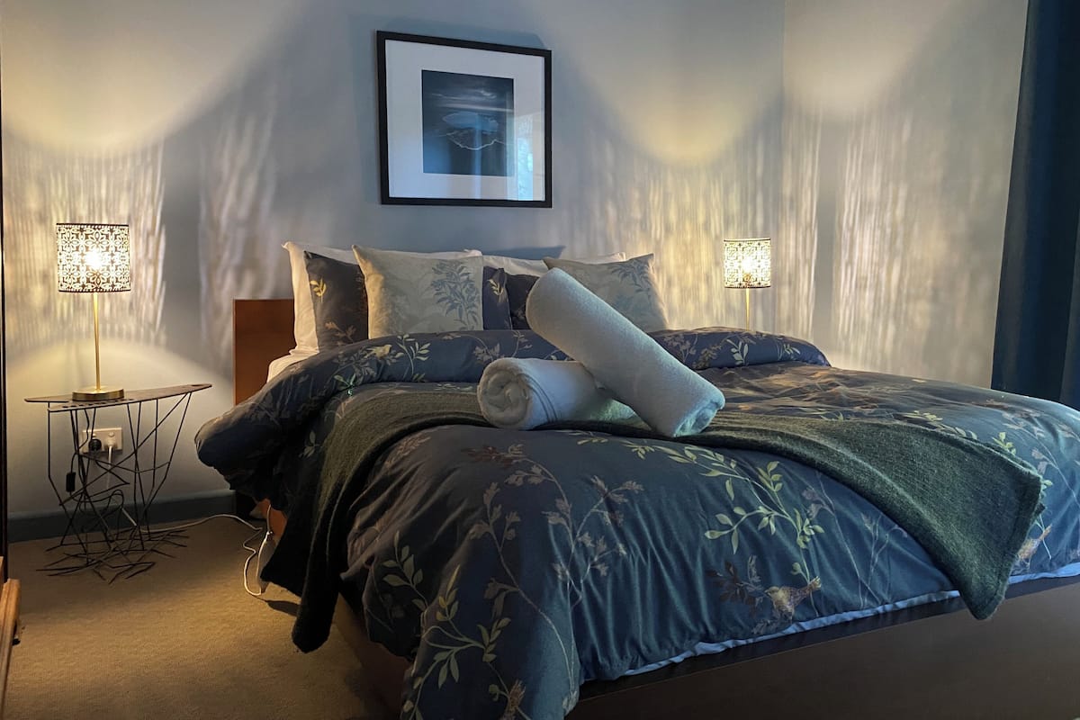 A neatly made bed with floral bedding, two bedside lamps, and a framed picture on the wall.
