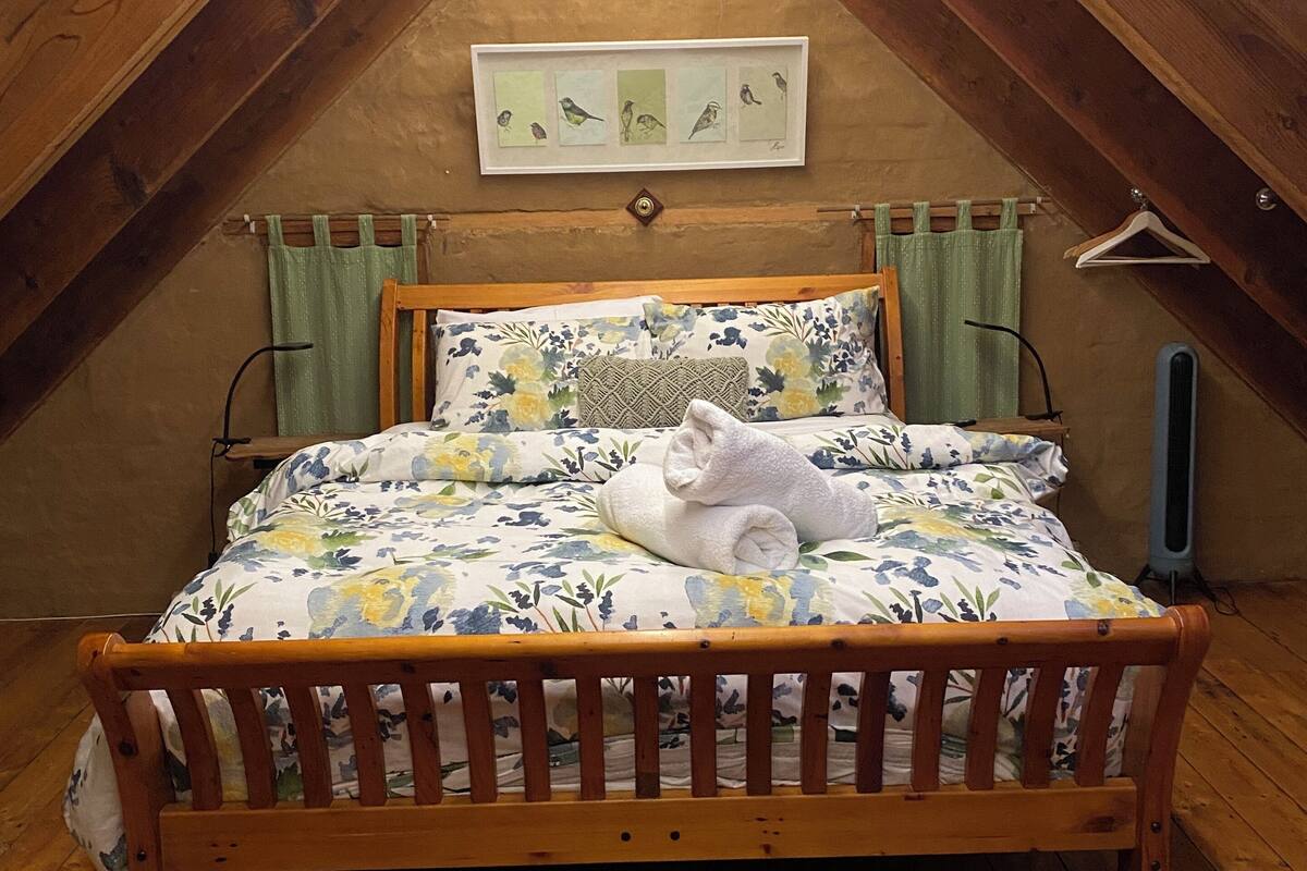 A cozy attic bedroom with a wooden bed, floral bedding, and a framed bird artwork on the wall.