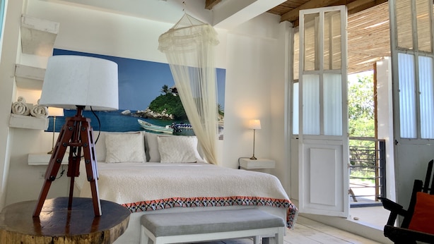 Une chambre à coucher avec un lit, une lampe sur pied, un ventilateur de plafond, une grande fenêtre et une vue sur la mer.