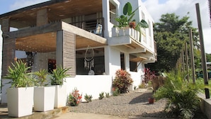 Une maison moderne à deux étages, dotée d’un balcon, de plantes en pot et d’une allée gravillonnée.