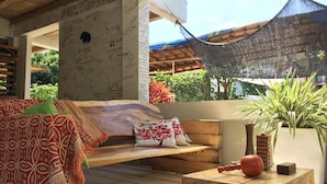 Un espace extérieur accueillant, aménagé avec un banc en bois, un canapé confortable et une petite table agrémentée d’un vase et d’un objet décoratif.