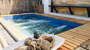 Un bain à remous avec une terrasse en bois, et une assiette remplie de coquillages et de morceaux de bois flotté.