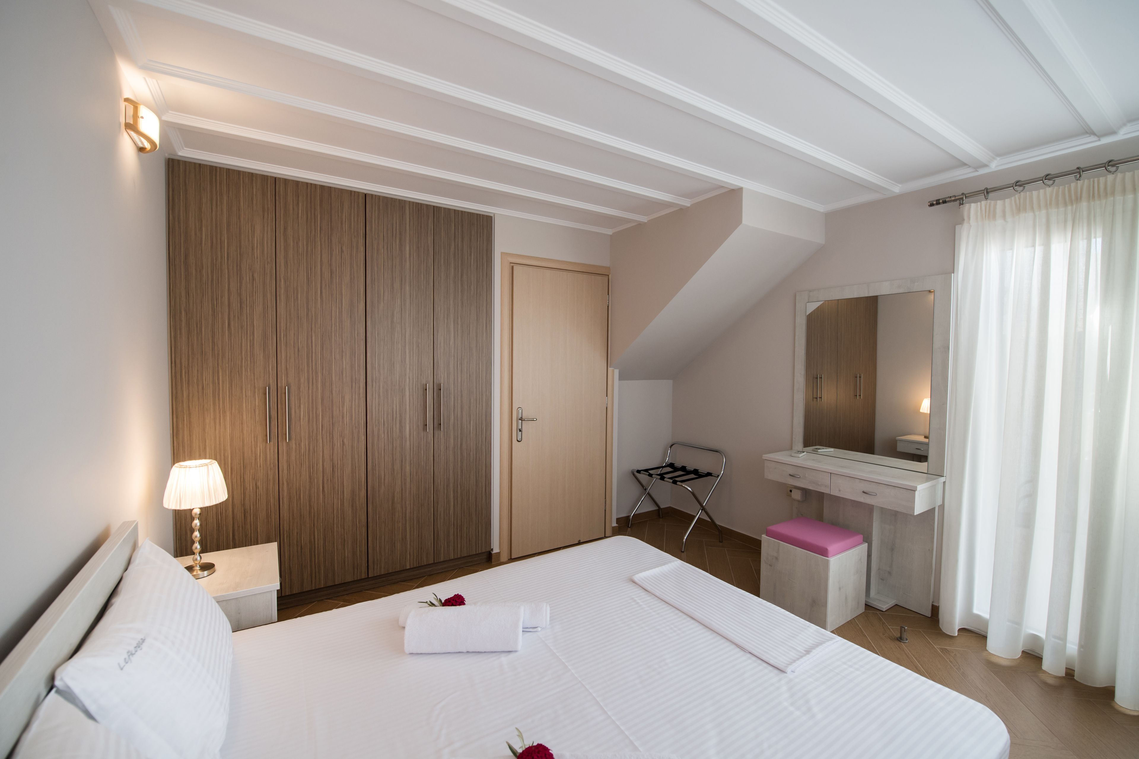 Habitación de hotel con una cama grande, un armario de madera, un tocador con espejo y una pequeña zona de estar.