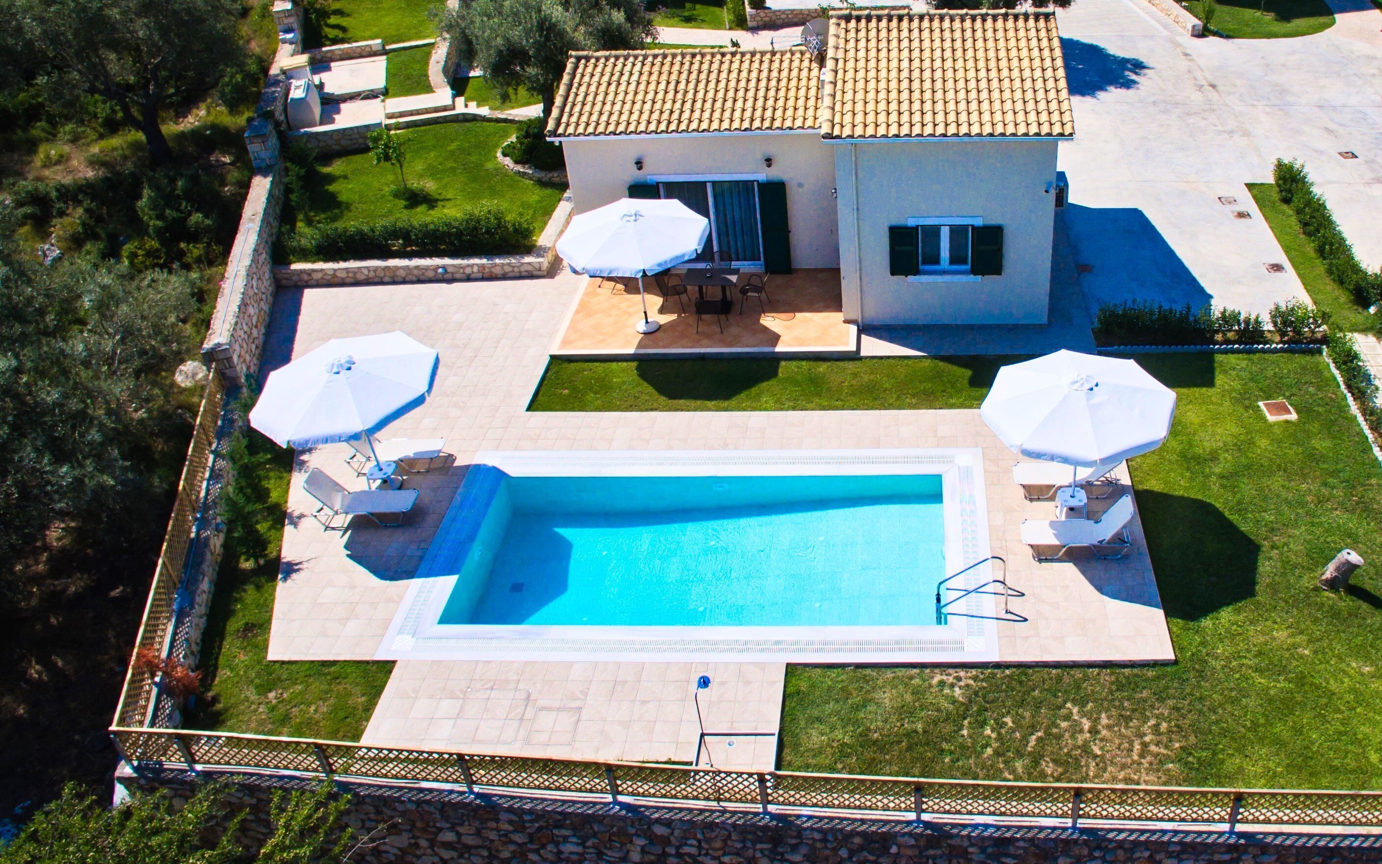 A residential property with a swimming pool, two umbrellas, and a patio area.