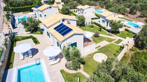 Et boligområde med flere huse, hvert med swimmingpool, solpaneler og udendørs siddepladser.