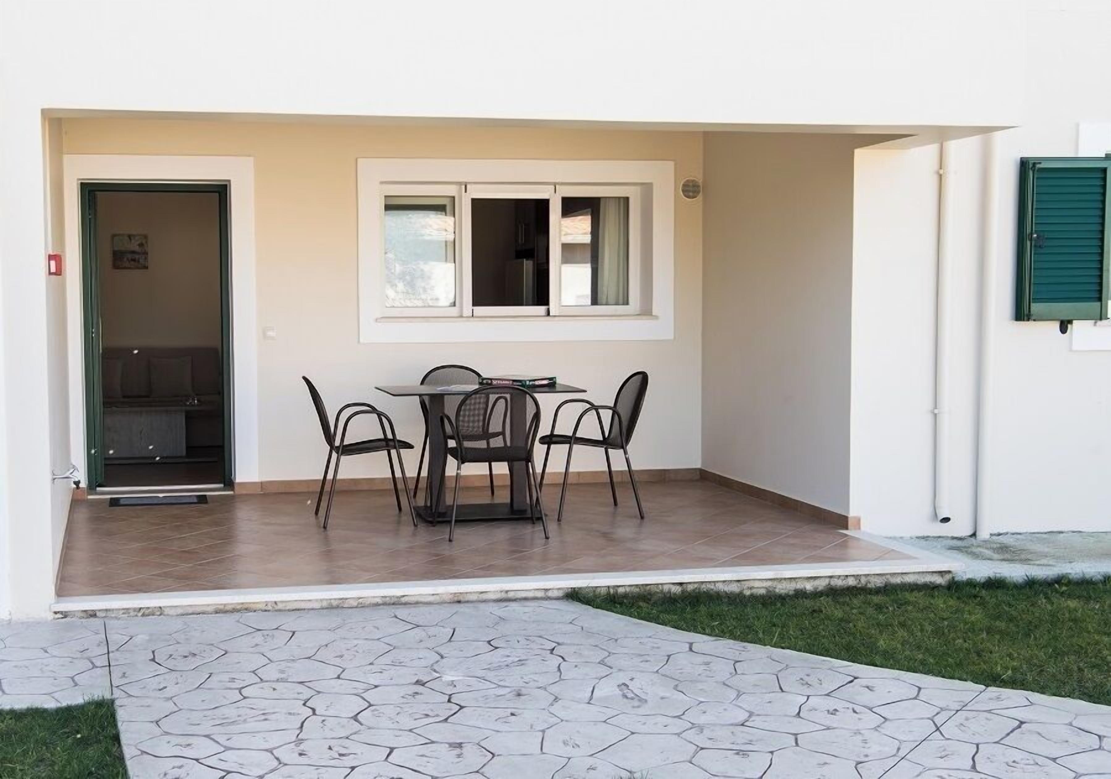 A patio with a table and chairs, a door leading to an interior space, and a window with shutters.