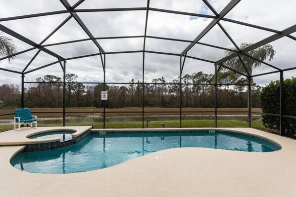 A swimming pool with a curved edge, surrounded by a covered area with a metal frame and glass panels.