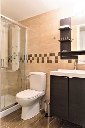 A modern bathroom with a glass-enclosed shower, a white toilet, a sink with a dark cabinet, and a tiled backsplash. - Heraklion Urban Apartments - Adults Only (Heraklion)