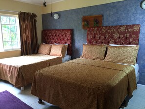 Una habitación con dos camas, cada una con una colcha estampada y almohadas a juego. Hay una ventana con cortinas, un reloj de pared y un plato decorativo sobre las camas.