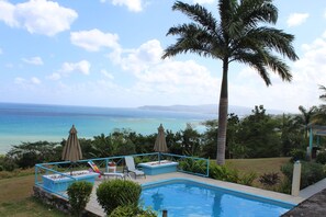 A pool with a view of the ocean, surrounded by lounge chairs and umbrellas. - Free Transportation. Private Villa.  Amazing Ocean View, Pool, And housekeeper. (roundhill)