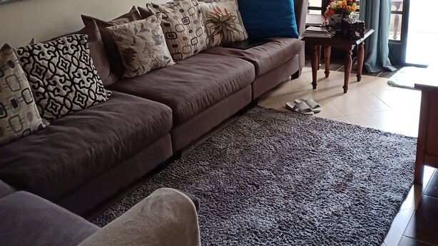 Un salon avec un canapé marron, des coussins à motifs, un tapis foncé, une horloge et une fenêtre avec des rideaux.