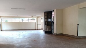 Une pièce spacieuse et vide, dotée d’un sol carrelé, d’une porte avec une grille métallique et d’une fenêtre protégée par une rambarde en métal.