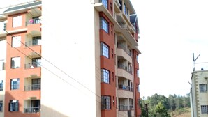 Un immeuble résidentiel à plusieurs étages, doté de balcons, d’une allée pavée et surplombant un paysage vallonné.