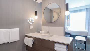 Un baño moderno con tocador de madera, un espejo redondo y un ventanal con cortinas.