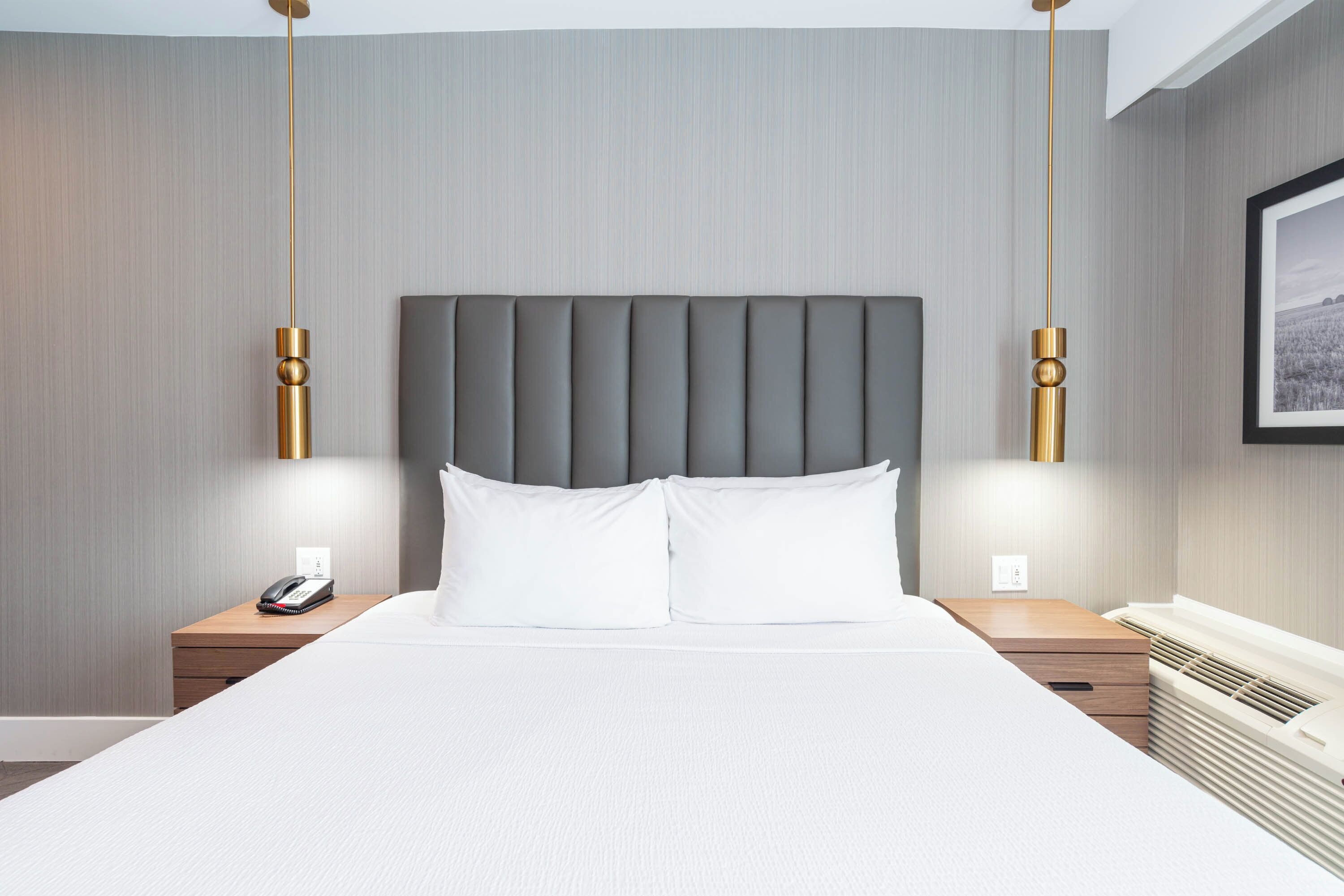 Una habitación de hotel moderna con una cama grande, dos mesitas de noche, un teléfono en la pared y un cuadro enmarcado.