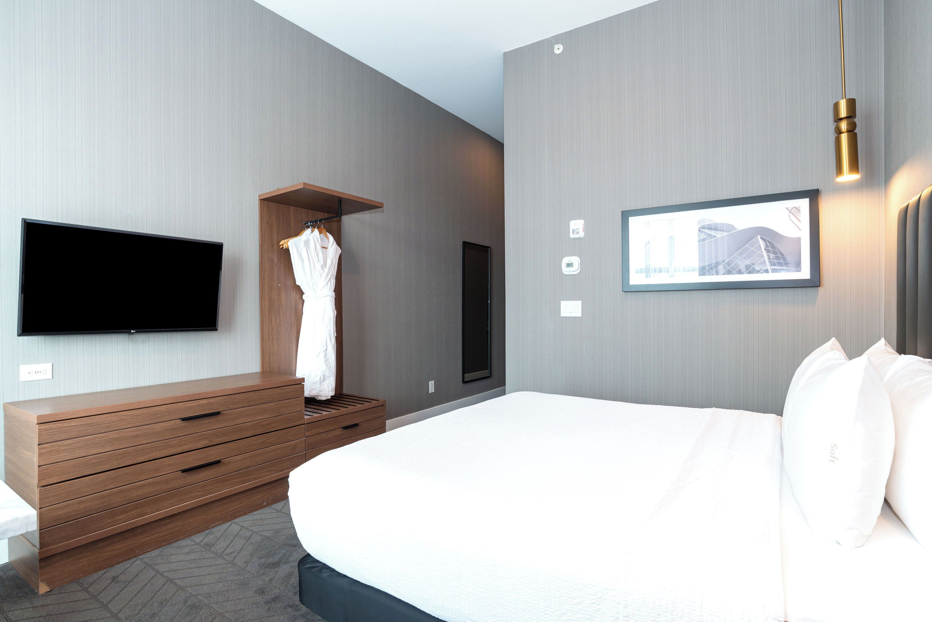 Una habitación de hotel moderna con una cama grande, un aparador de madera, un televisor de pantalla plana y un cuadro en la pared.