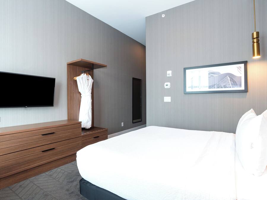 Ein modernes Hotelzimmer mit einem großen Bett, einer Holzkommode, einem Flachbildfernseher und einem gerahmten Bild an der Wand.
