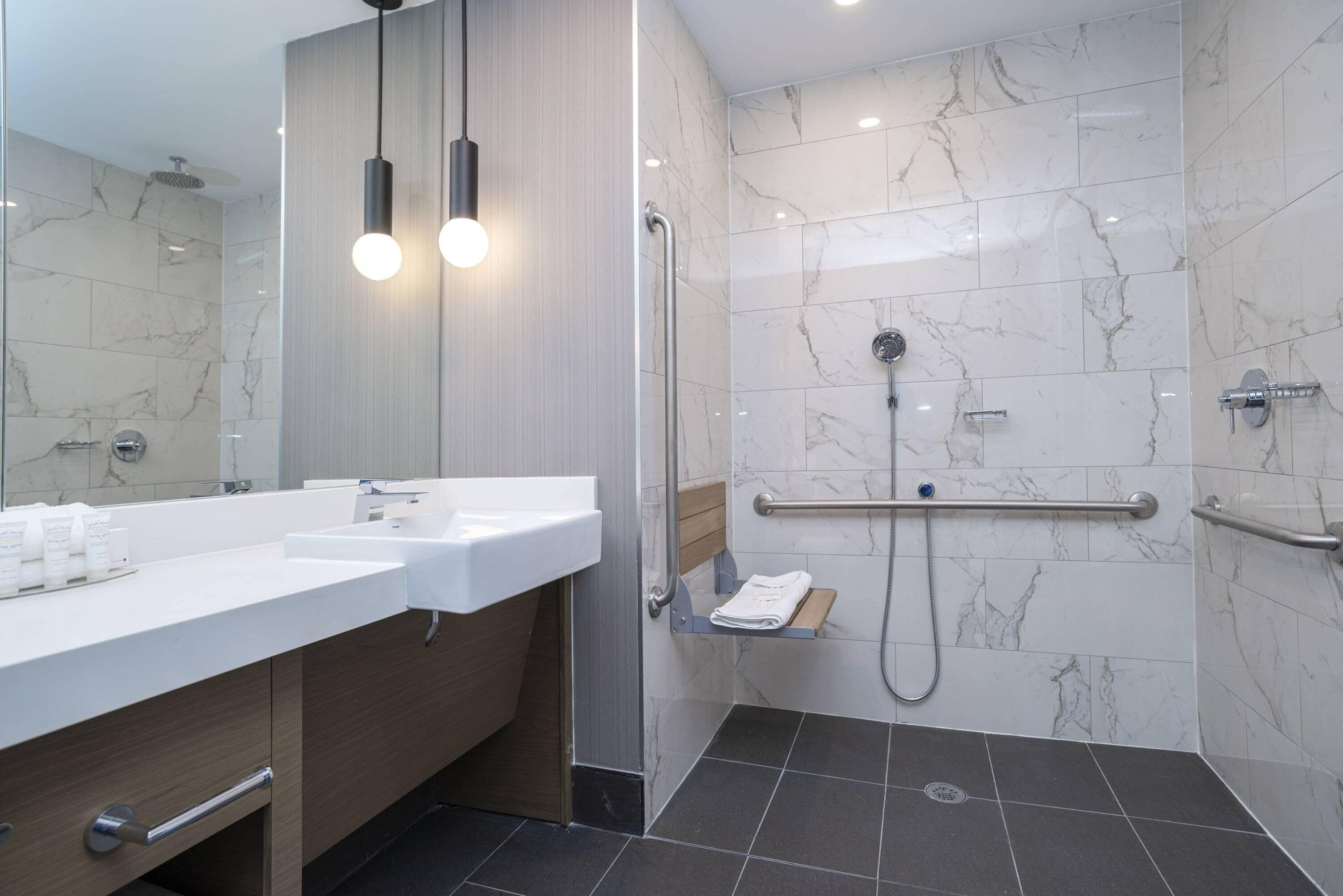 A modern bathroom with a dual sink vanity, a walk-in shower with a handheld showerhead, and a grab bar for safety.