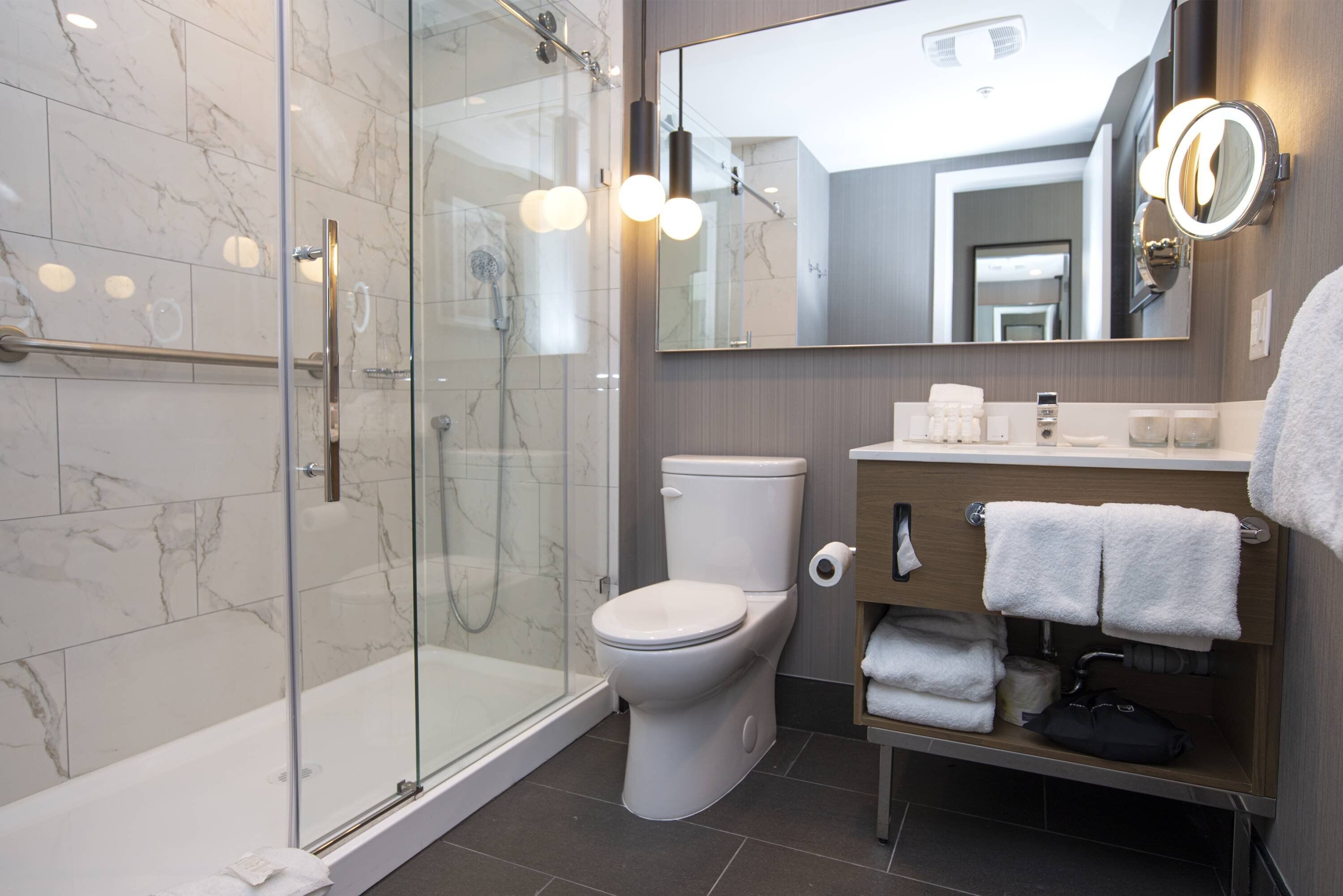 Une salle de bain moderne avec une douche à parois de verre, des toilettes, un meuble-lavabo avec un miroir et des serviettes soigneusement rangées.