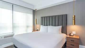 A modern hotel room with a large bed, a bedside table, a nightstand, and a wall-mounted telephone.