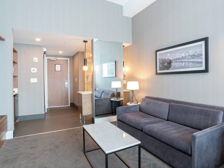 Een moderne hotelkamer met een grijze bank, een klein tafeltje, een spiegel en een inlijsting foto aan de muur.