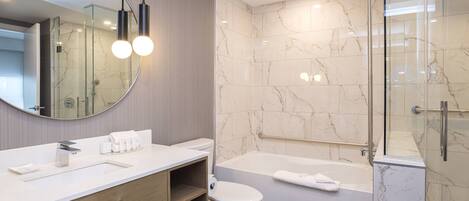 Un baño moderno con pared de azulejos de mármol, ducha con mampara de vidrio, lavamanos blanco y bañera.