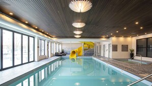Een binnenzwembad met een gele glijbaan, grote ramen en een modern plafond.