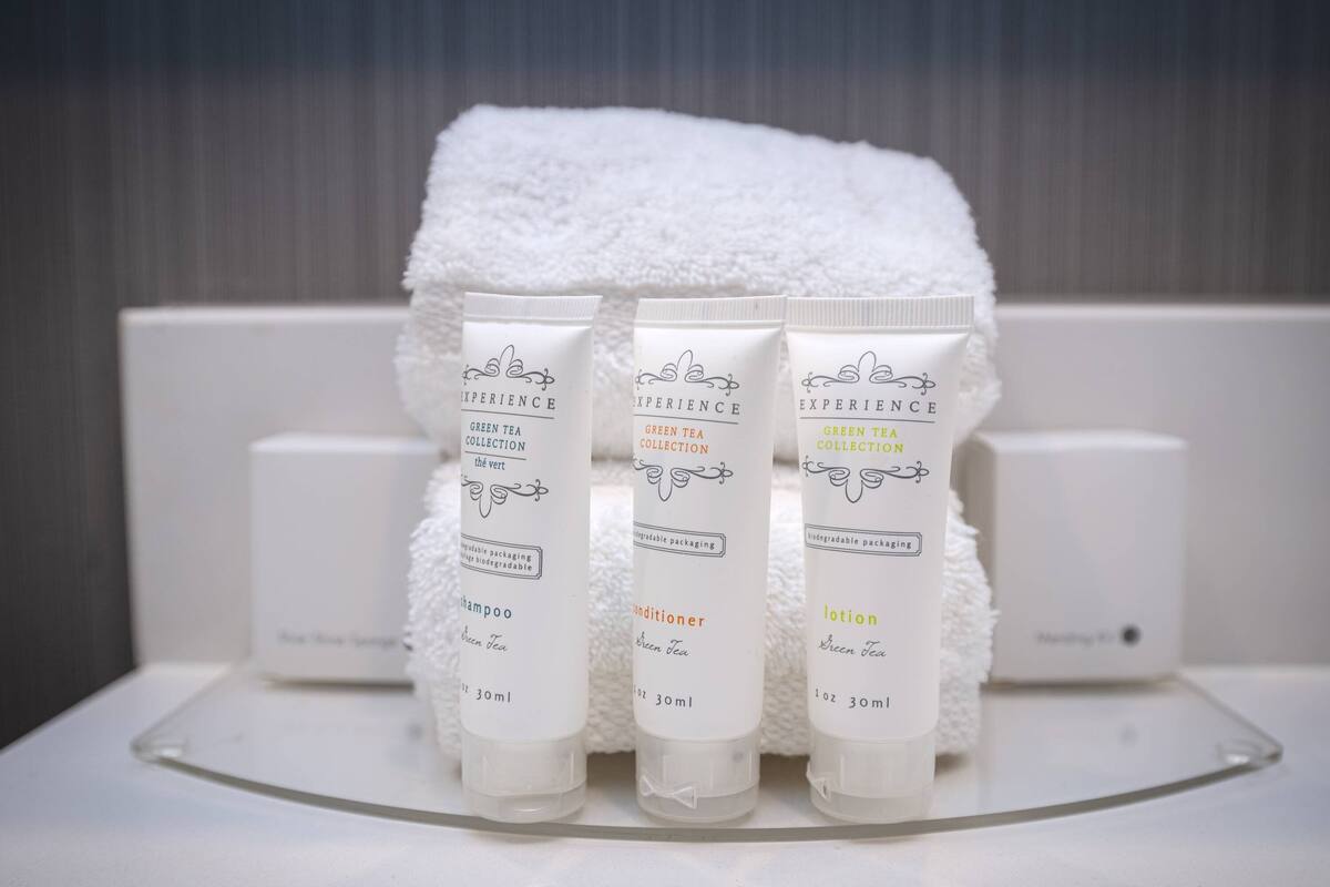 Trois flacons de produits de toilette étiquetés « Collection thé vert » sont posés sur une surface blanche, avec une serviette blanche en arrière-plan.