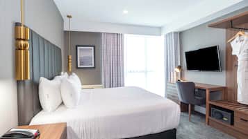 Habitación de hotel con una cama grande, un escritorio, una silla, un televisor y un armario.